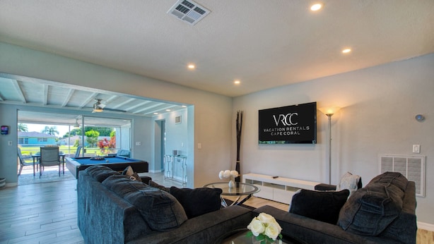 A modern living room with a pool table, comfortable seating, and a sign for vacation rentals.