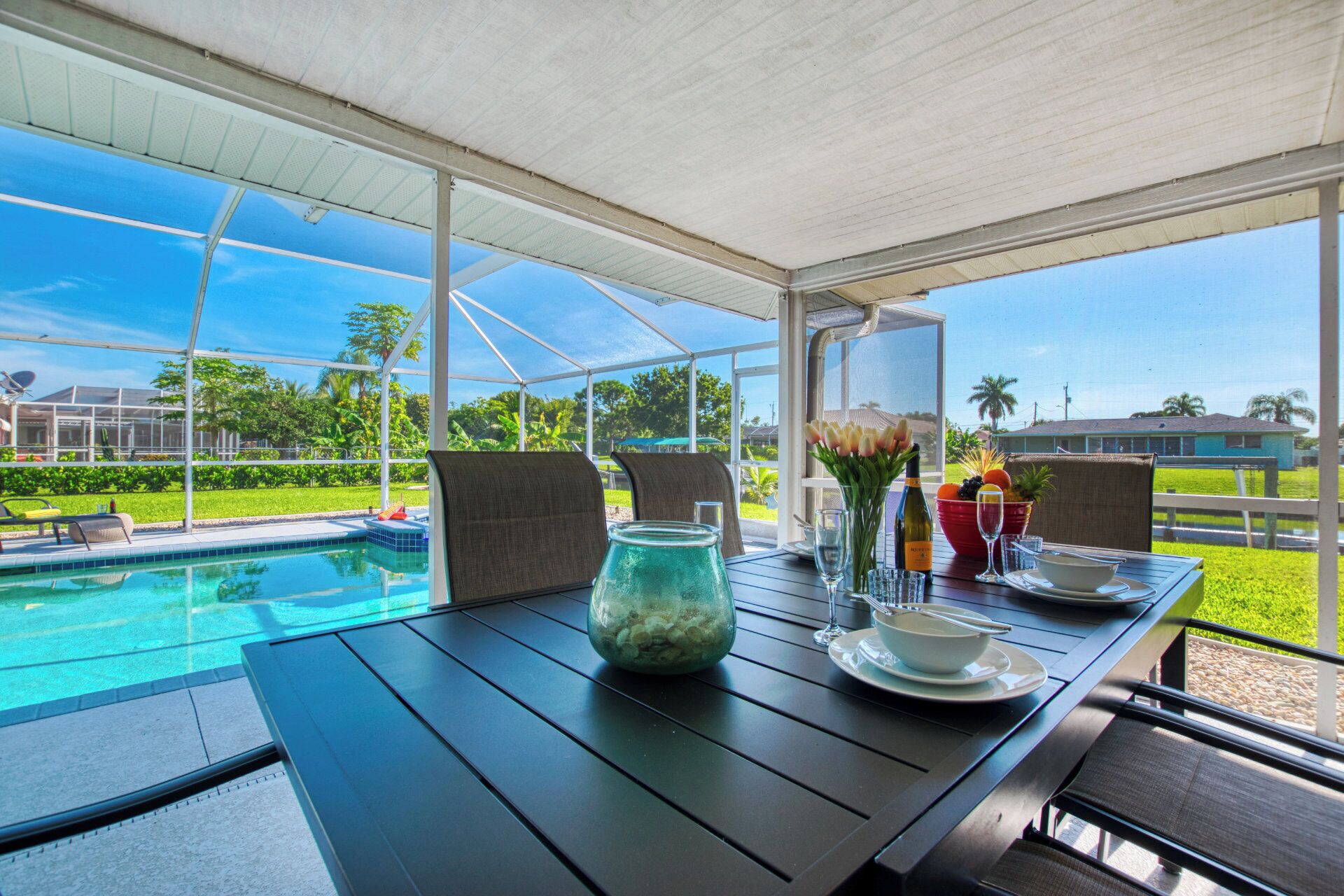 Un espace extérieur abrité, aménagé pour les repas, avec vue sur la piscine, une table dressée avec une carafe, des verres et un saladier.