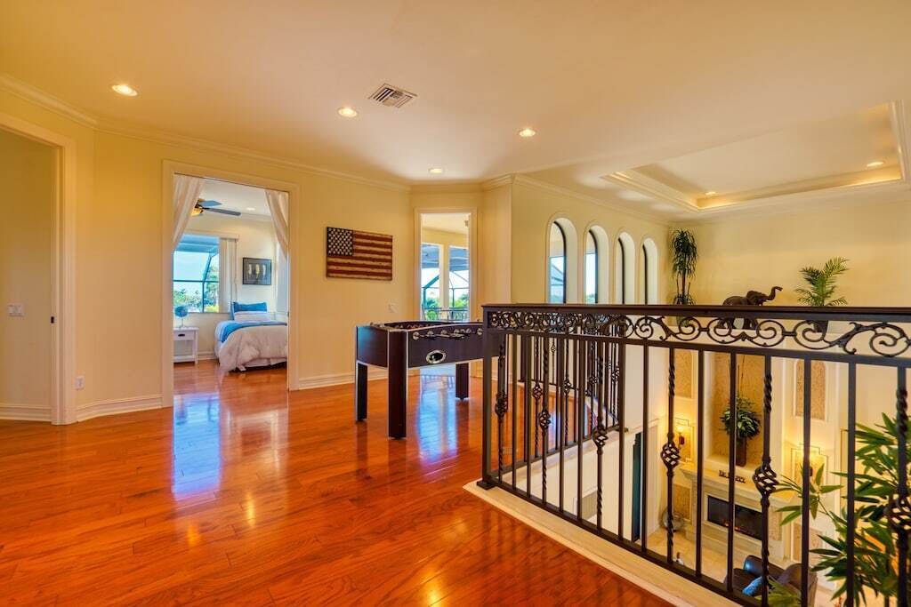 A spacious room with hardwood floors, a bed, a foosball table, and a balcony with a railing.