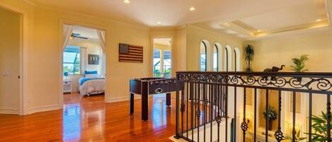 A spacious room with hardwood floors, a bed, a foosball table, and a balcony with a railing.