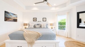 Una camera da letto con un letto, due comodini, una ventola a soffitto, una finestra con tende e vista sul verde.