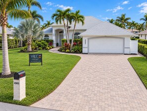 A modern two-story house with a garage, surrounded by well-maintained lawns and palm trees.