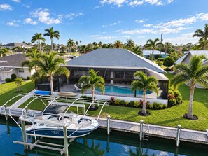 A modern house with a swimming pool, docked boat, and lush landscaping.