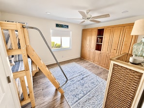 Una habitación con literas, armarios de madera, un ventilador de techo y una ventana.