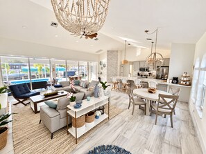 A modern living room with a large window, a dining area, and a kitchen with stainless steel appliances.