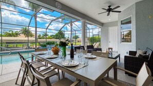 Ein Essbereich mit Blick auf den Pool, einem Deckenventilator und einem großen Fenster.