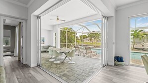 A spacious indoor area with a pool view, a dining area with chairs, and a ceiling fan. - VRCC Villa Nouveau - 4 bedrooms, pool and spa (Cape Coral)