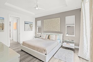 Une chambre à coucher moderne avec un grand lit, des tables de chevet, un ventilateur de plafond et des œuvres d’art accrochées aux murs.