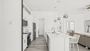 A modern kitchen with white cabinetry, a central island, and a dining area with a white table and chairs. - VRCC Villa Nouveau - 4 bedrooms, pool and spa (Cape Coral)