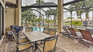 A covered outdoor area with a pool, seating, and a view of palm trees.