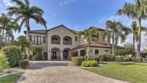 A two-story house with a paved driveway, palm trees, and a well-maintained lawn.