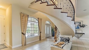 A spacious living room with a curved staircase, large windows, and a sofa with decorative pillows.
