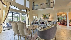 A spacious living room with a high ceiling, elegant furniture, and large windows offering a view of the outdoors.