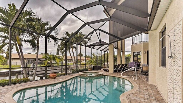 A swimming pool with a covered area, palm trees, and outdoor furniture.