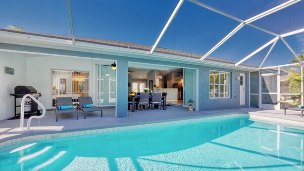 Ein Swimmingpool mit überdachter Terrasse, Grill und Essbereich.