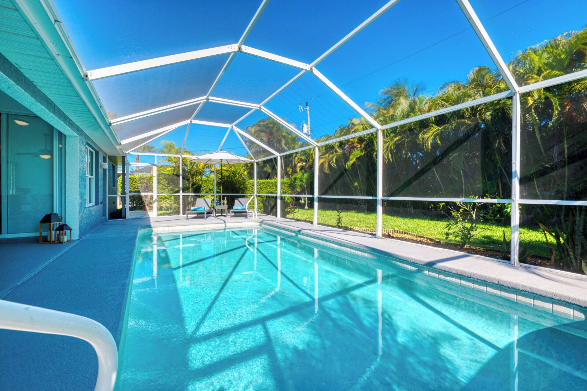 Una piscina cristalina con cerramiento de vidrio, rodeada de follaje y un edificio de fachada azul.