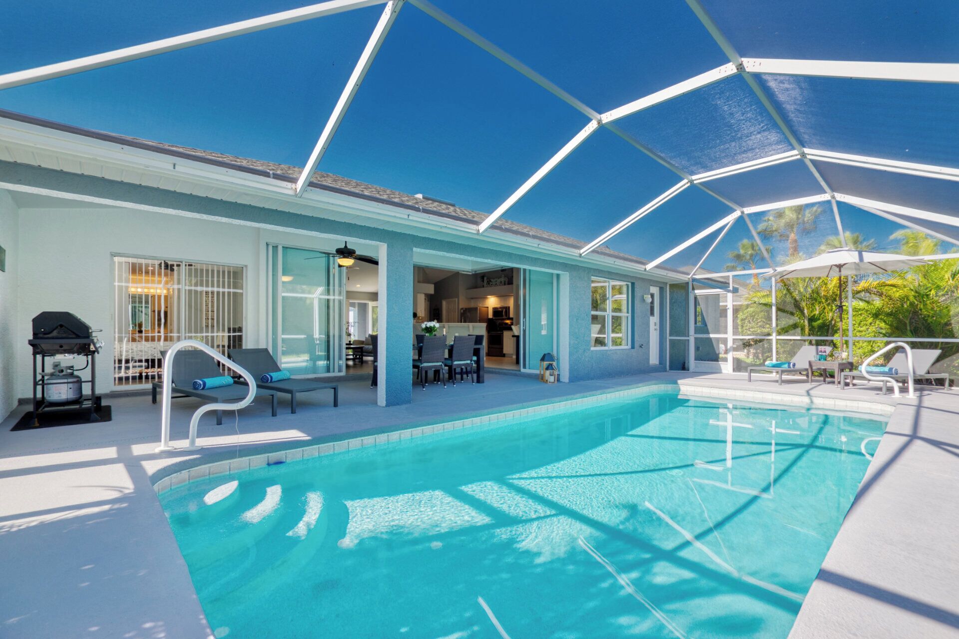 A swimming pool with a covered area, lounge chairs, and a barbecue grill.
