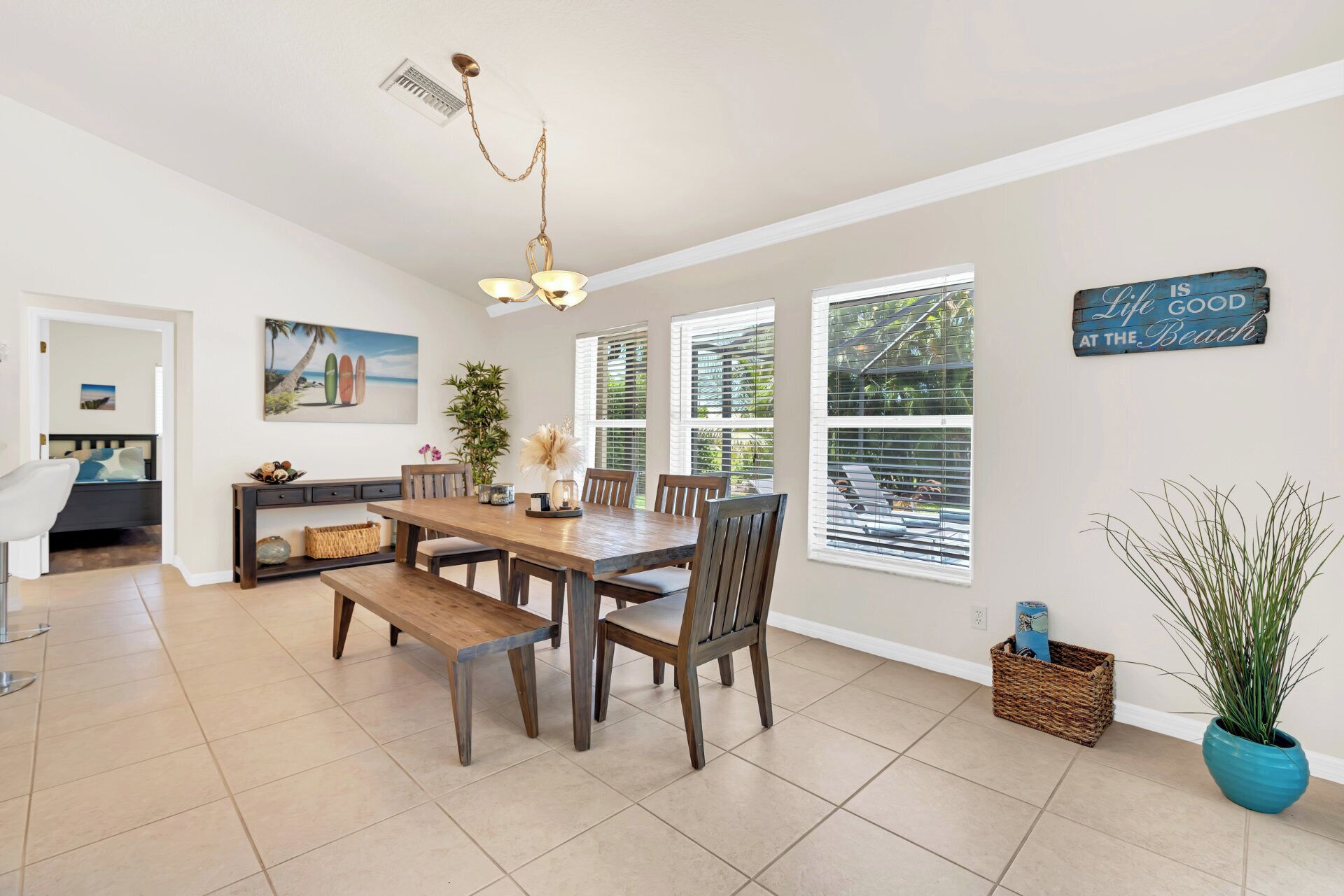 A spacious dining area with a wooden table and chairs, a bench, a ceiling fan, and a large window with blinds.