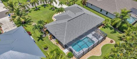 Vista aérea de un barrio residencial con casas, piscina y palmeras.