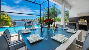 Ein Essbereich mit Blick auf einen Swimmingpool und das Meer, inklusive Grill und Tisch, der für eine Mahlzeit gedeckt ist.