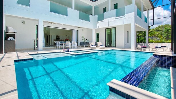 Ein modernes Haus mit einem großen Schwimmbad, einer überdachten Terrasse und einem Essbereich mit Gartenmöbeln.