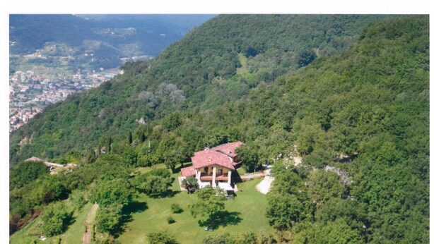 A large house with a red roof surrounded by lush greenery and hills.
