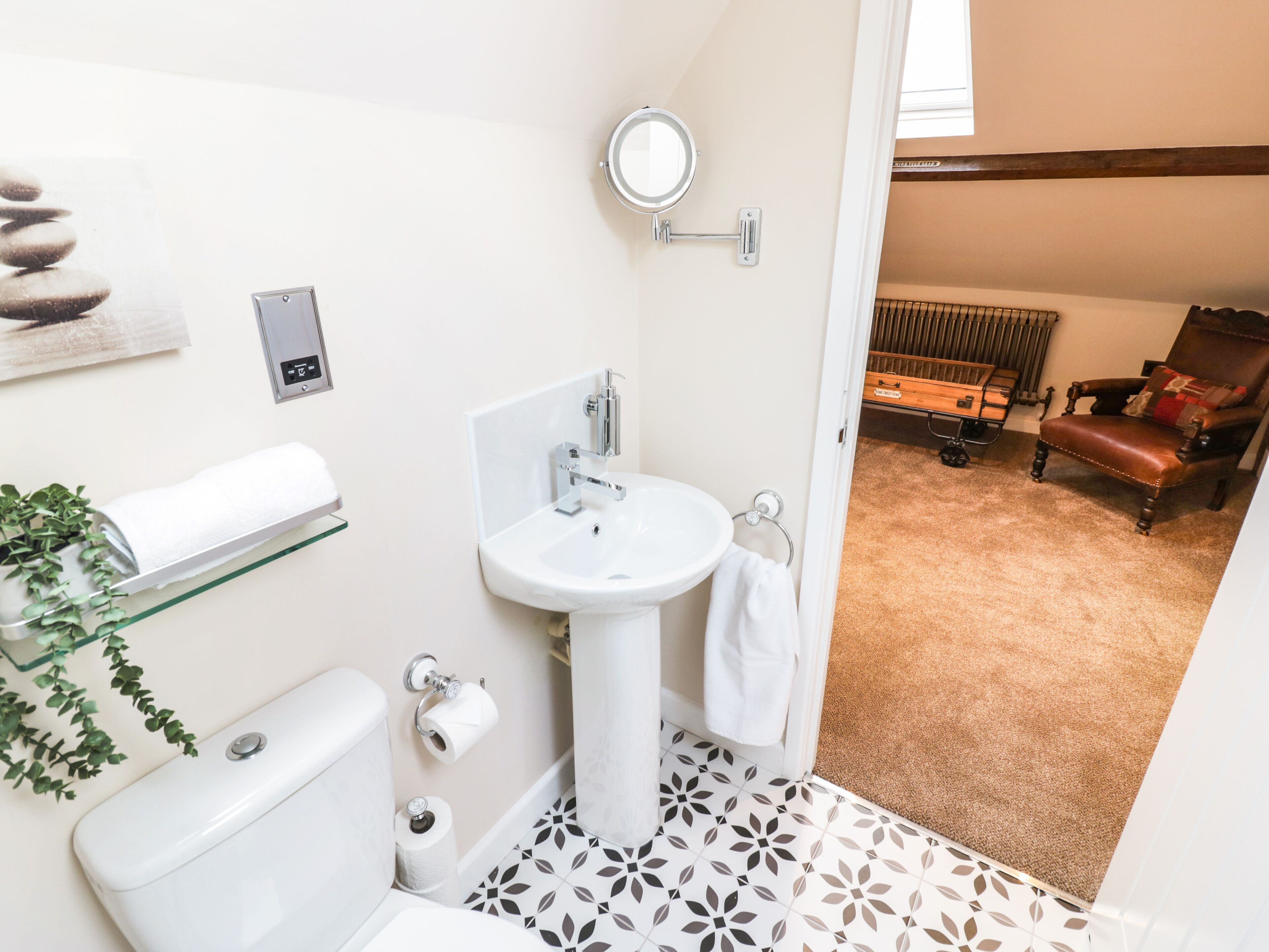 A bathroom with a toilet, sink, and towel rack. There is a mirror on the wall and a plant on the left. The floor has patterned tiles.