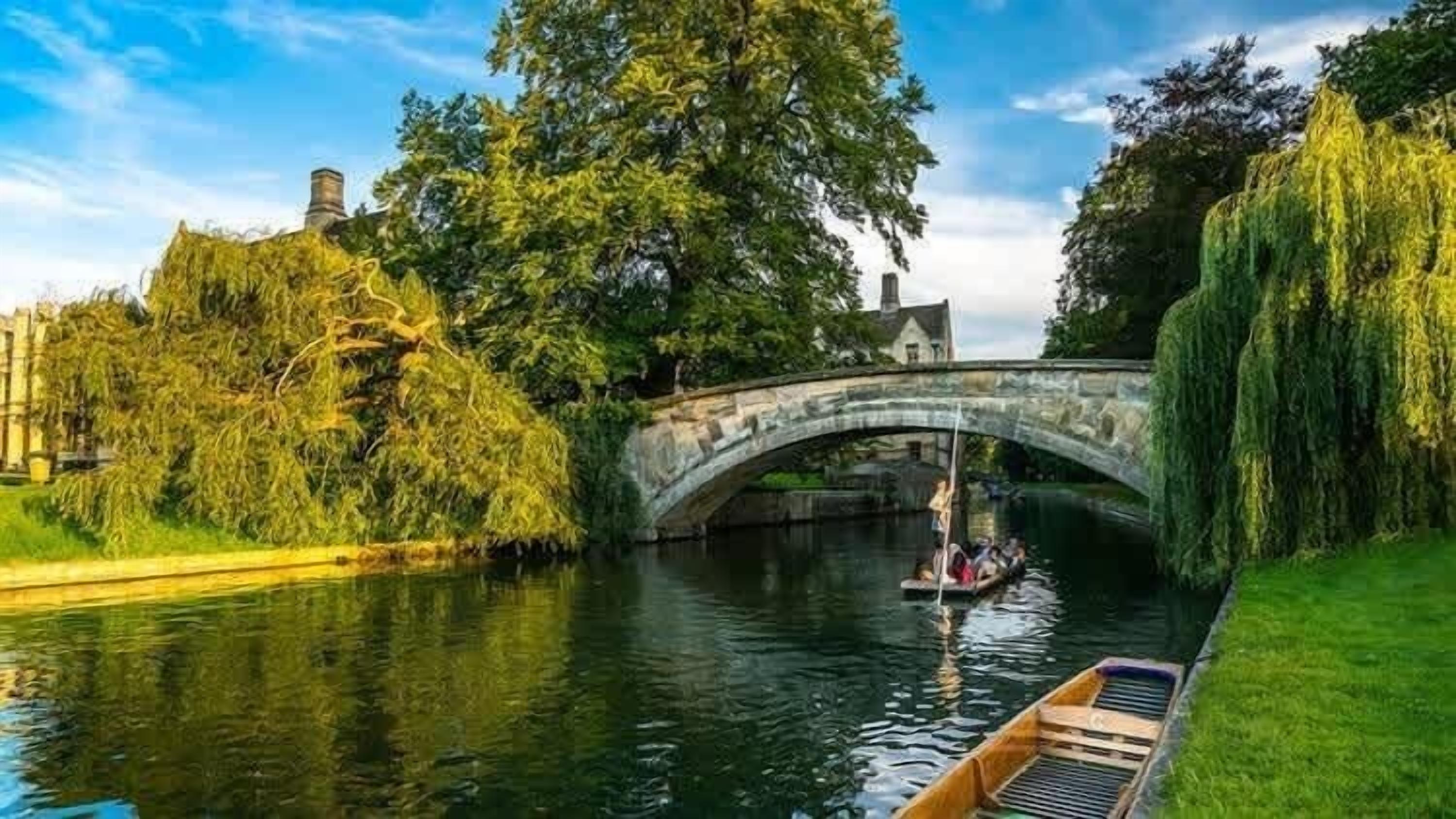 A stone bridge over a calm river, surrounded by lush greenery and trees.
