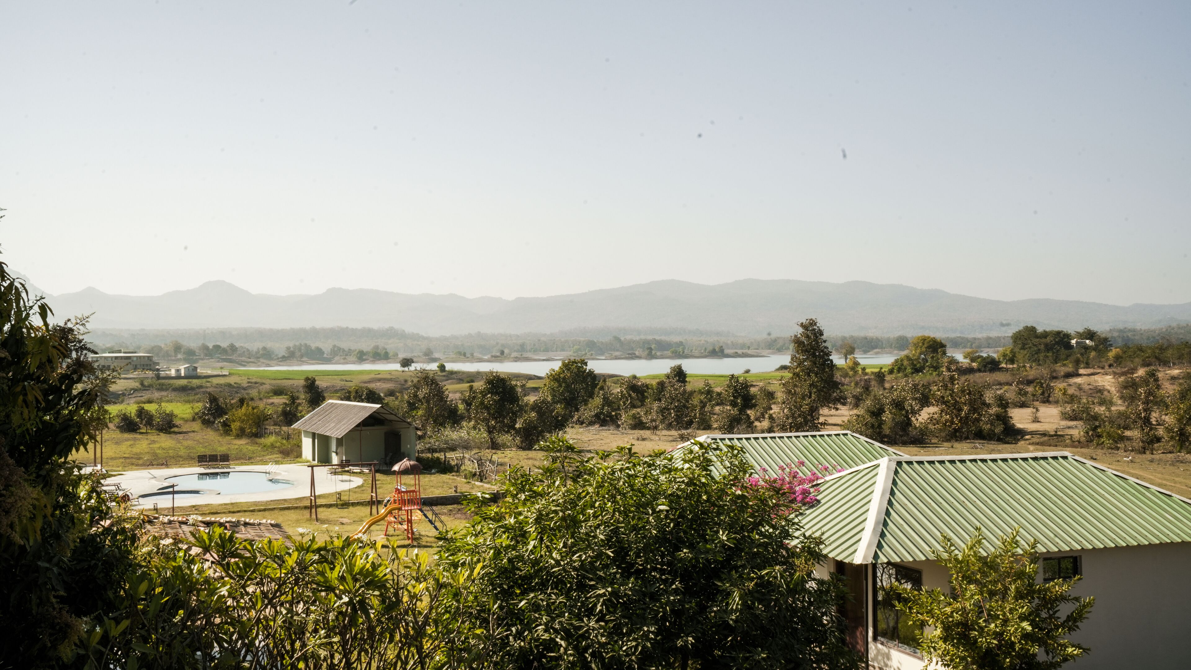A view of a property with a swimming pool, a small building, and a green-roofed structure.