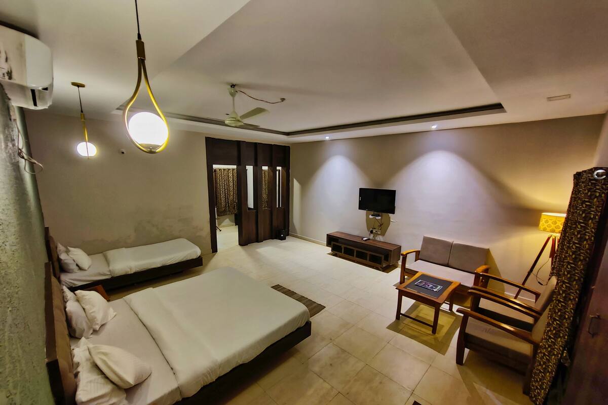 Ein Hotelzimmer mit zwei Einzelbetten, einem Sofa, einem Fernseher, einem kleinen Tisch und einem Deckenventilator.
