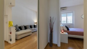 Un apartamento moderno con sala de estar, un dormitorio, un armario blanco y un jarrón decorativo.