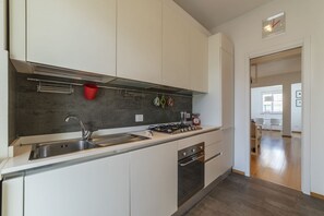 Eine moderne Küche mit weißen Schränken, einer Edelstahl-Spüle, einem Gasherd und einem roten Wasserkocher.