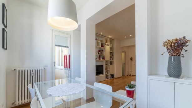 Una cocina moderna con una mesa de comedor de vidrio, armarios blancos y una estantería empotrada.