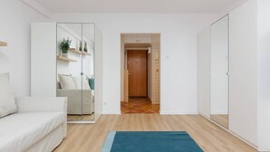 Una sala de estar moderna y minimalista con un sofá blanco, un tapete azul y un separador de vidrio con estantes.