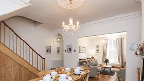 Ein Essbereich mit einem Holztisch, gedeckt für vier Personen, eine Treppe und ein Wohnzimmer mit Sofa und Fenster.