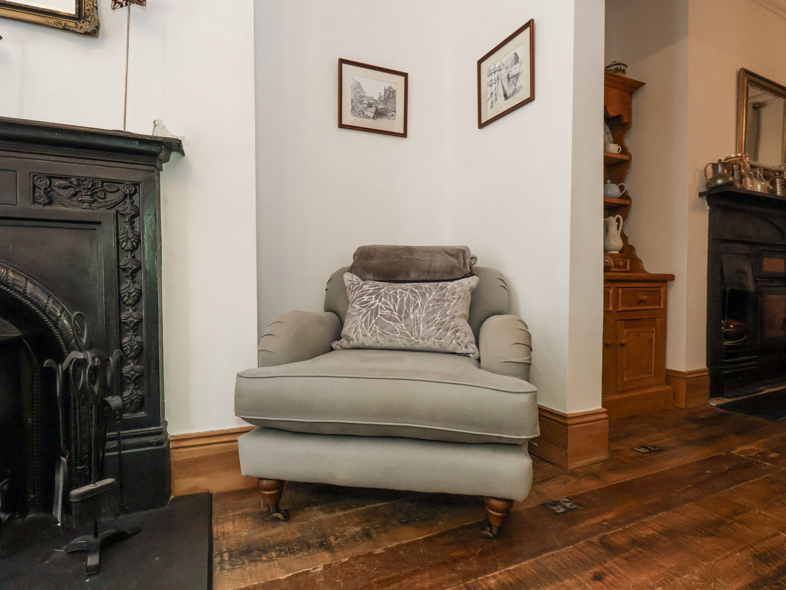 A room with a grey armchair, a fireplace, and two framed pictures on the wall.