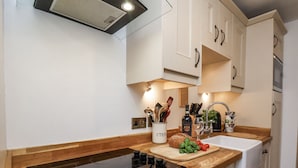 Eine moderne Küche mit schwarischem Induktionskochfeld, Holz Arbeitsplatte, weißen Schränken und einem eingebauten Backofen.