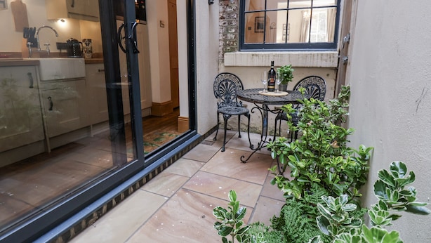 Eine Küche mit Glastür zu einer Terrasse, auf der sich Tisch und Stühle sowie ein Blumentopf befinden. Ein Fenster bietet Blick ins Innere.