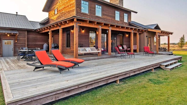 A wooden house with a deck, outdoor seating, and a covered patio area. - Luxury Family Home with Full Teton Views + Hot Tub (Driggs)