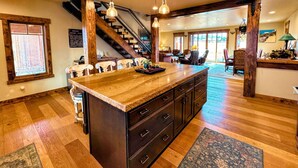 A spacious kitchen with a large island, wooden flooring, and a staircase leading to an upper level. - Luxury Family Home with Full Teton Views + Hot Tub (Driggs)
