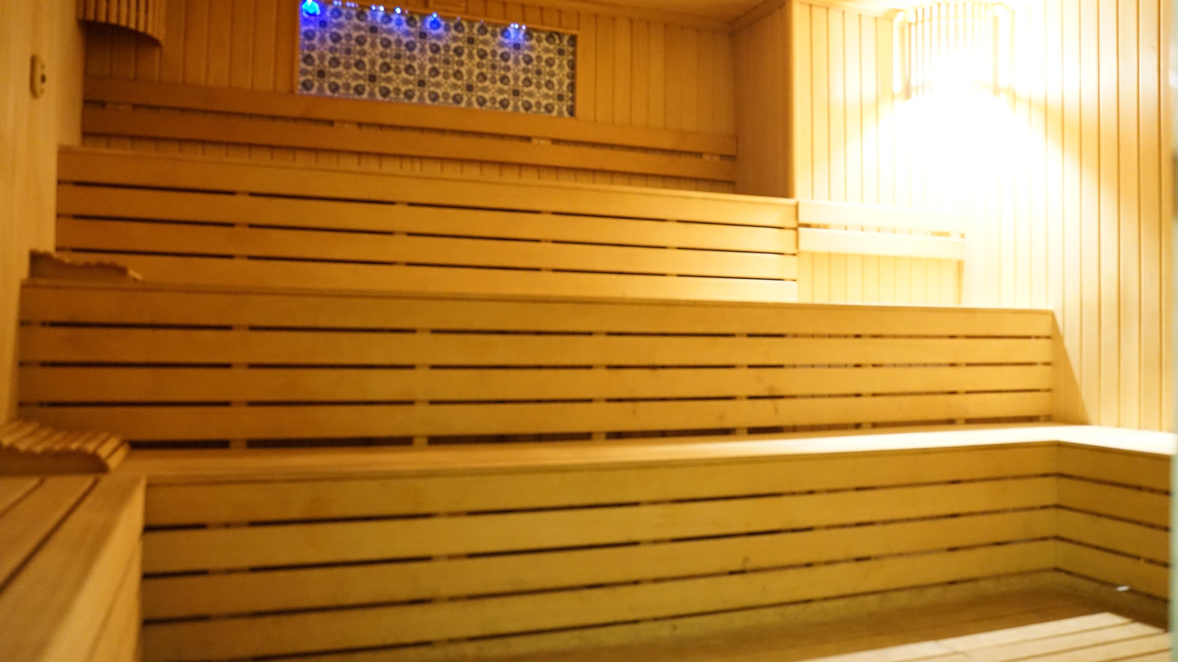 A row of wooden benches in a sauna area with a patterned window above.