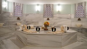 A spa area with a marble floor, a central seating area with towels and a fruit bowl, and decorative wall sconces. - Melid Hotel (Malatya)