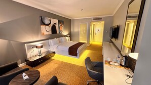 A hotel room with a bed, bedside table, lamp, chair, desk, and a TV. - Melid Hotel (Malatya)