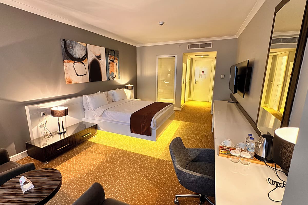 A hotel room with a bed, bedside table, lamp, chair, desk, and a TV.