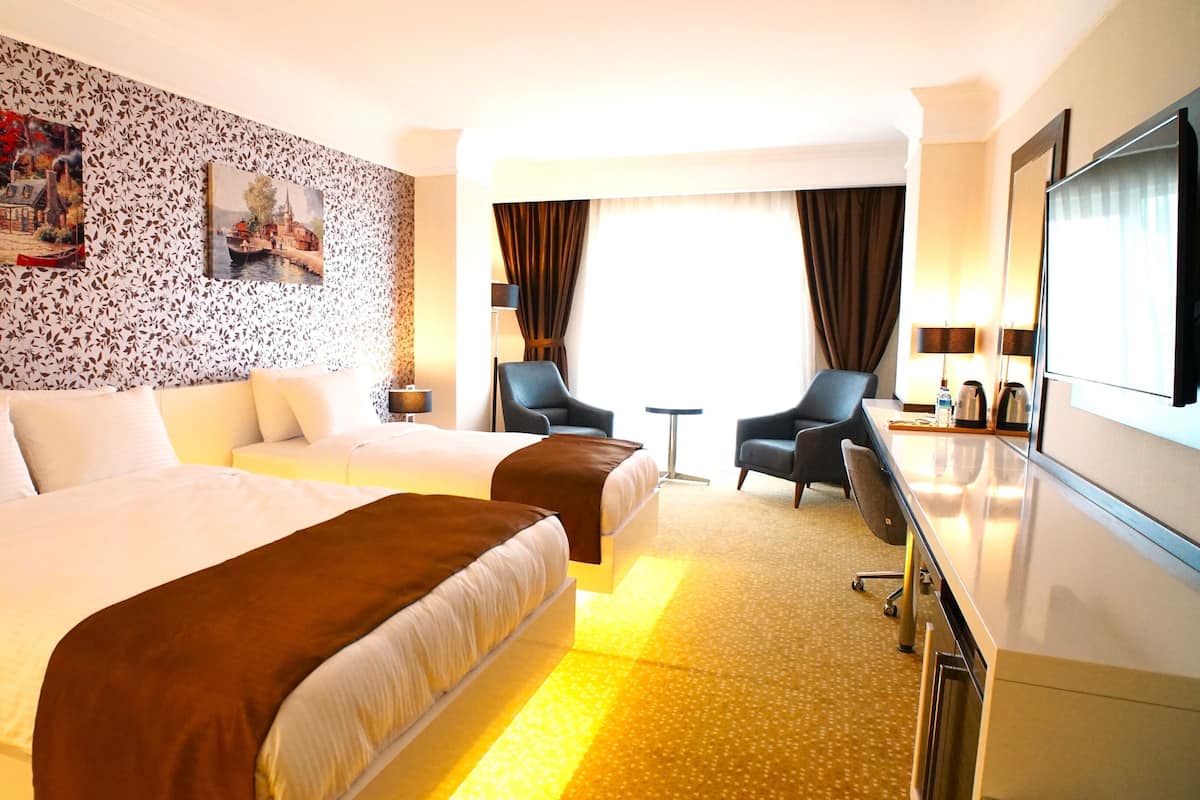 A hotel room with two beds, a desk, a chair, a TV, and a painting on the wall.