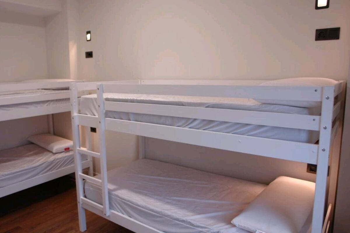 A bunk bed room with white bedding and a ladder.
