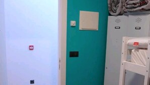 A room with teal walls, a wooden floor, a white door, a white wardrobe, and a white shelf unit. - Hostel Trovadores (Burgos)