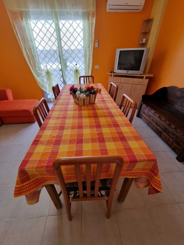 A dining area with a checkered tablecloth, wooden chairs, a flower centerpiece, and a TV on a stand.