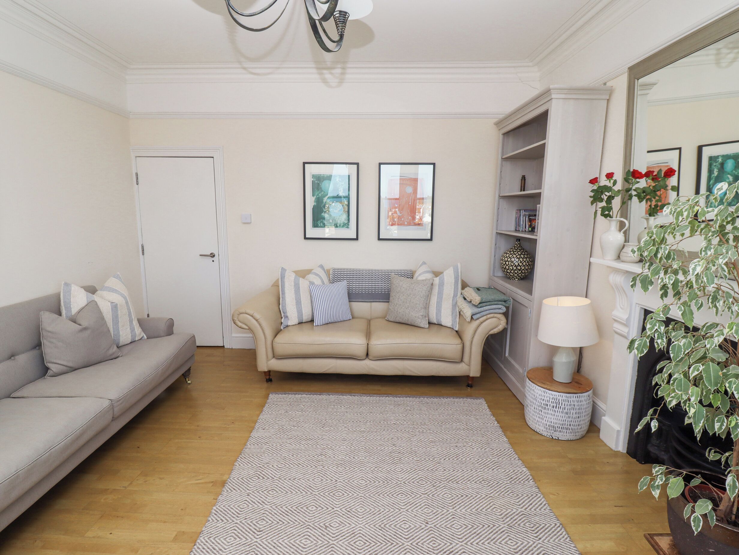 Ein Wohnzimmer mit einem beigefarbenen Sofa, einem gemusterten Teppich und einem Bücherregal mit Dekorationselementen.