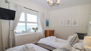 A hotel room with two beds, a TV, a window with curtains, a wooden nightstand, and artwork on the wall. - Whistler (St Ives)